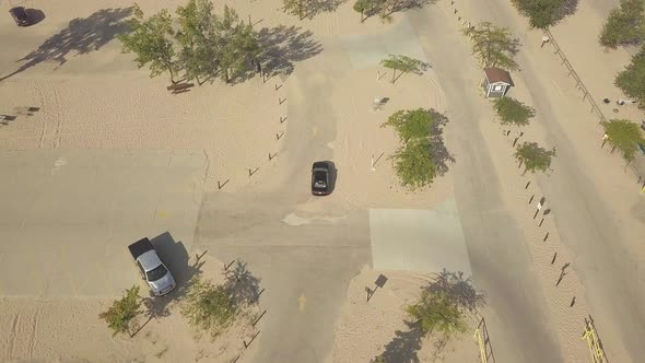 Aerial view of a black car driving through the parking lot at a sandy beach campground.