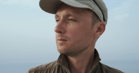 Caucasian Man Traveler in Cap Peers Into Distance Against Blue Sky in Day Time Closeup