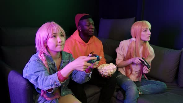 Indoor Shot of a Group of Interracial Millenial People Playing Video Games Sitting on a Dark Sofa