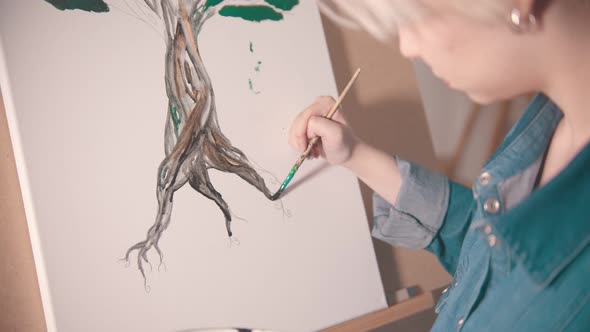 A Young Woman with Short Hair Painting Tree Trunk in Darker Color