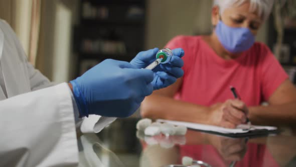 Male doctor visiting senior mixed race woman preparing vaccination