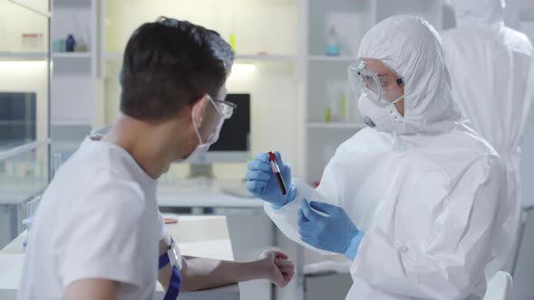 Doctor in Protective Gear Showing Blood Sample to Patient