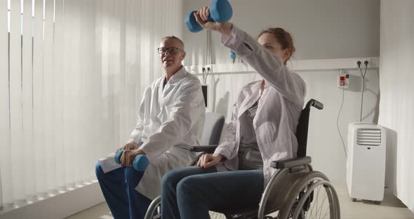 Physiotherapist Helping Young Woman in Wheelchair Exercising with Dumbbells