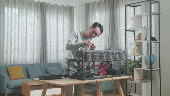 Asian Man Wearing Glasses Connects The Power Cords Of Mining Rig For Mining Cryptocurrency