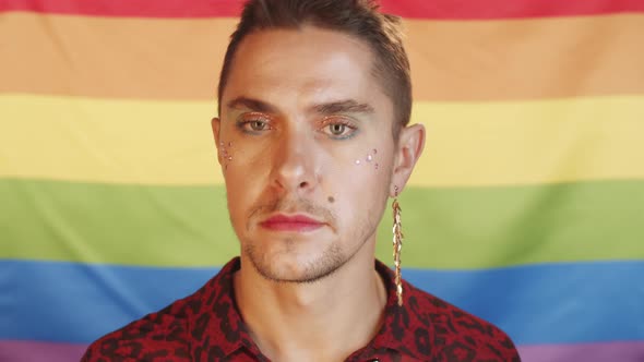 Gay Man with Makeup Posing against Rainbow Flag