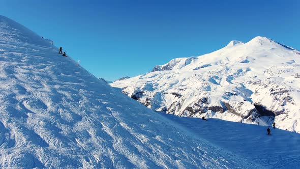 Men Silhouettes Ski on Snowy Mountain Slope Under Blue Sky