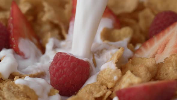 Corn flakes with raspberry and strawberry in a bowl pouring with milk. Slow Motion.