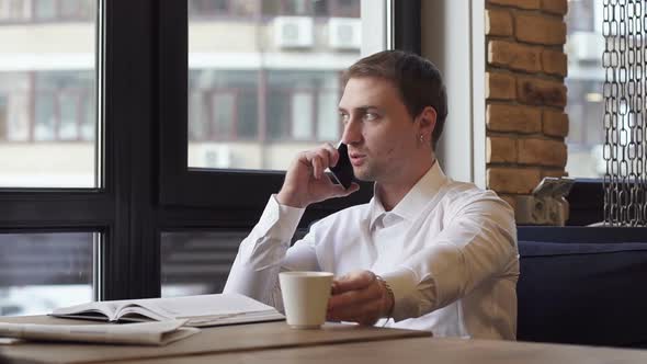 Businessman Talking on the Phone in a Cafe and Drinking Coffee