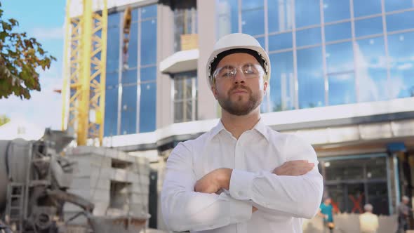 An Engineer in a White Shirt and Helmet Stands Against the Backdrop of a Modern Glass Building