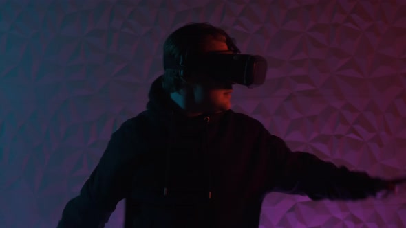 Close Up View Man in Black Hoodie and VR Helmet on His Head Move Left and Right and Puts His Hands