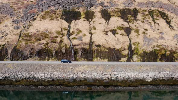 Drone Shot Of Car Driving On Road Next To Mountainside And Fjord