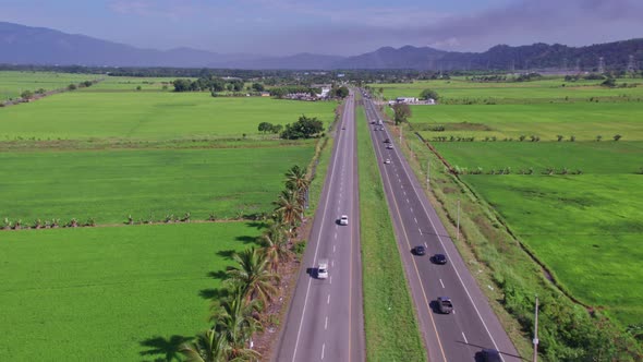 Aerial flyover motorway with traffic on Bonao surrounded by green growing rice fields and dark cloud