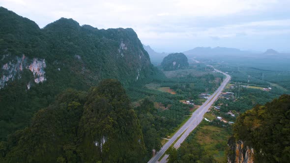 Aerial View of the Road with Driving Cars and Trucks Between High Mountains with Jungle Palm Trees