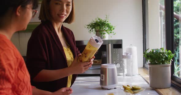 Asian mother and daughter preparing healthy drink in kitchen smiling