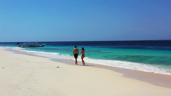 Two people tan on exotic tourist beach wildlife by blue green sea and white sand background of Bali 