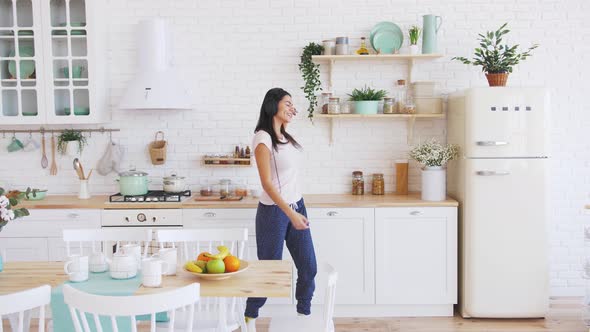 Young Happy Beautiful Woman Dancing in Kitchen Wearing Pajamas and Headphones and Listening to Music