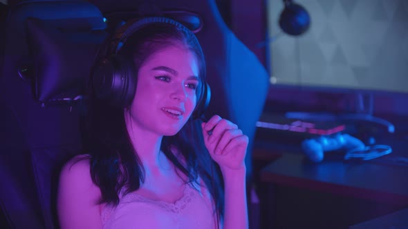Young Woman Sitting in Neon Gaming Club - Wearing Big Headphones and Talking in Microphone