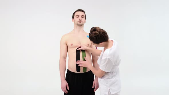 Female therapist applying kinesiology tape on a man's abdomen on the light background. 