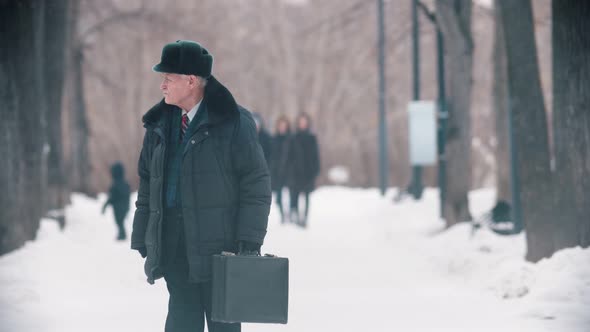 An Elderly Man with Bag Walking in the Park While Snowfall