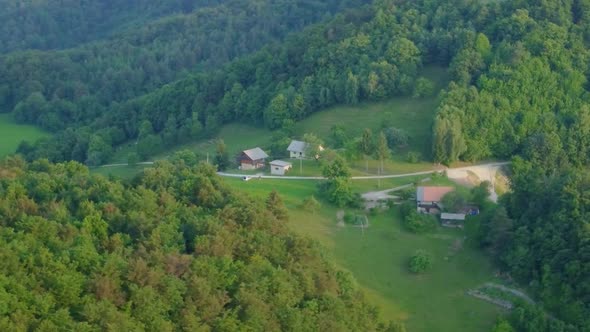 Farm houses up in hills surrounded with green meadows and spruce forest. Aerial round flight 4k view