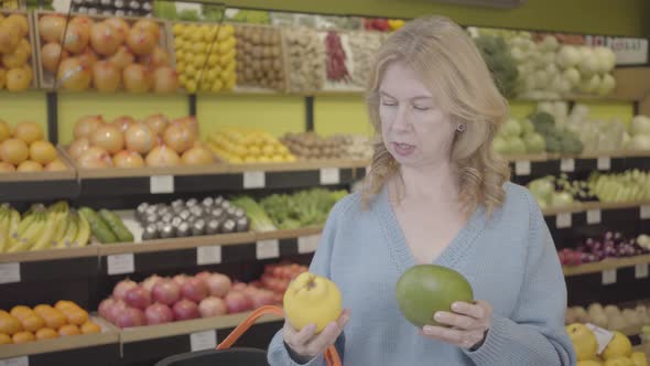 Portrait of Serious Caucasian Senior Woman Choosing Fruits in Grocery As Her Female Friend Coming