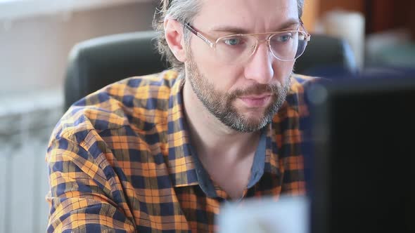 Middle Aged Man Works in an Office at a Computer. His Eyes Are Tired and He Takes Off His Glasses