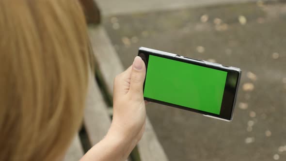 Blonde female in the park holding green screen smartphone 4K 2160p 30fps UltraHD footage - Woman sit