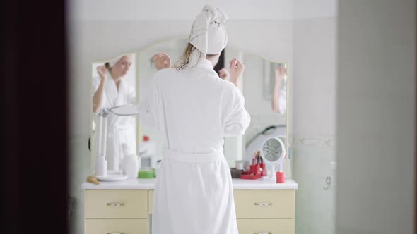 Back View of Slim Young Caucasian Woman in White Bathrobe and Hair Towel Dancing in Slow Motion in