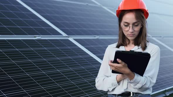 Beautiful young engineer standing near solar panels outdoors, Green Energy Concept.