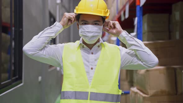 Asian young male engineer worker wearing protective face mask in warehouse factory during Covid19