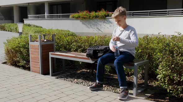 Blond Boy Takes a Plastic Bottle of Water From School Backpack and Drinks