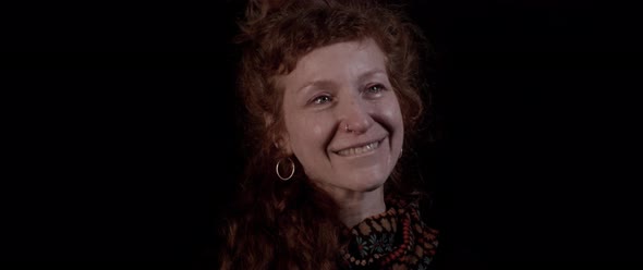 A woman with red hair bites her lip smiling in tears