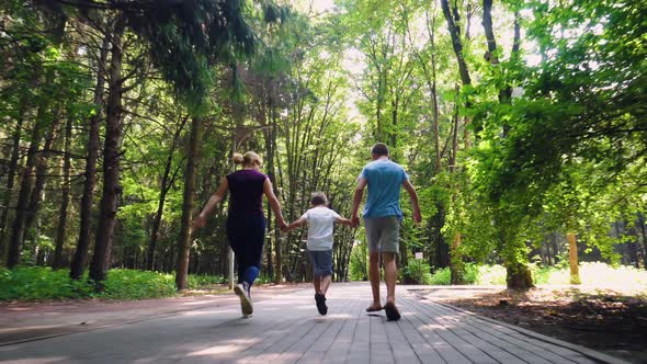 A Family of Three Runs Along an Alley in the Park