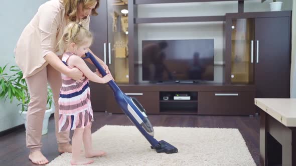 Mom Teaches Little Daughter to Clean Carpet in Room with Vacuum Cleaner