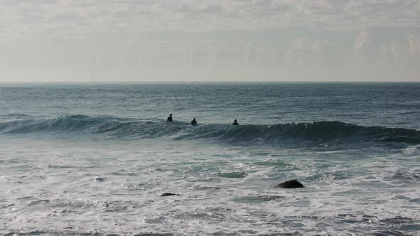 Three surfers sit in the line up waiting for a perfect wave in the dark blue pacific ocean water