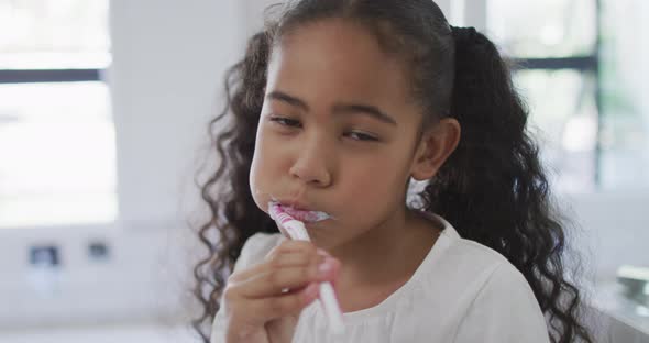 Portrait of happy biracial girl looking at camera and brushing teeth