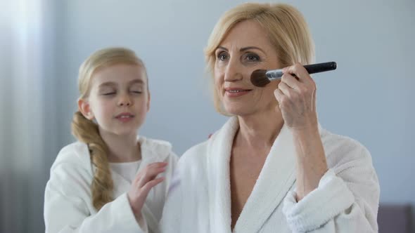 Little Girl Admiring Her Beautiful Grandmother Applying Face Powder, Beauty