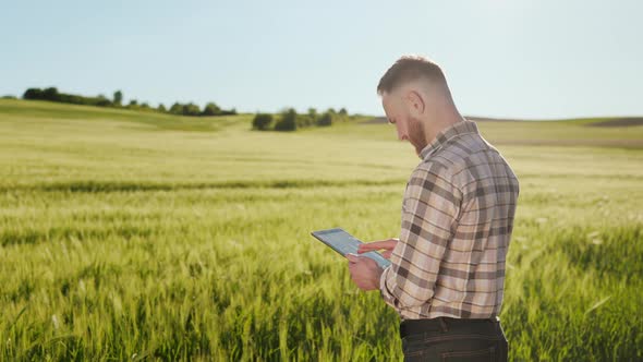 The Farmer is Standing Near the Field and Working with a Tablet