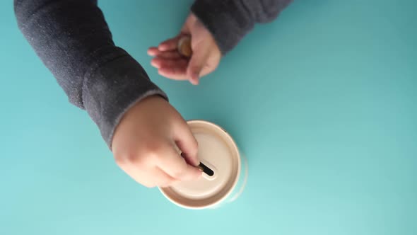 Child Hand Saving Coins in a Container on Light Green Background Top View