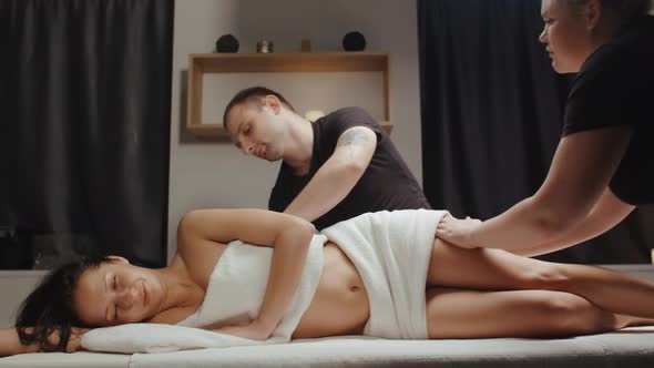 Slim Brunette Woman Receiving Body Rejuvenating Massage Procedure in Spa Pair of Massage Therapists