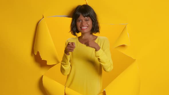 Young Woman Points at Camera and Says Hey You Picks Someone Yellow Background