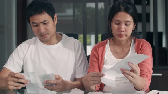 Young Asian Pregnant couple records of income and expenses at home. worried, serious, stress