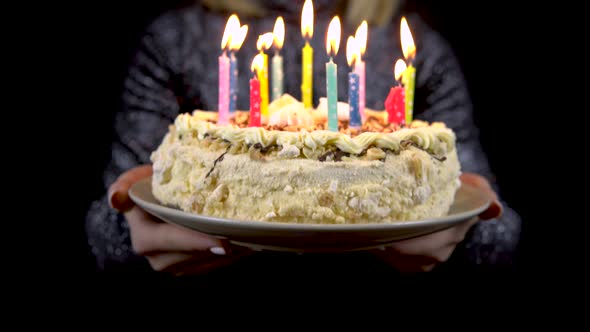 A Girl Holds Out a Holiday Cake with Candles Towards the Camera. Isolated Black Background