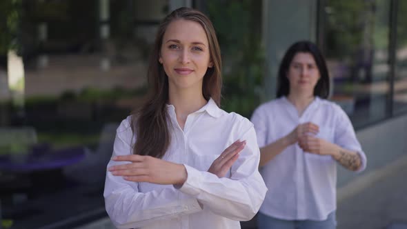 Beautiful Confident Woman and Blurred Friend at Background Crossing Hands in Slow Motion Looking at