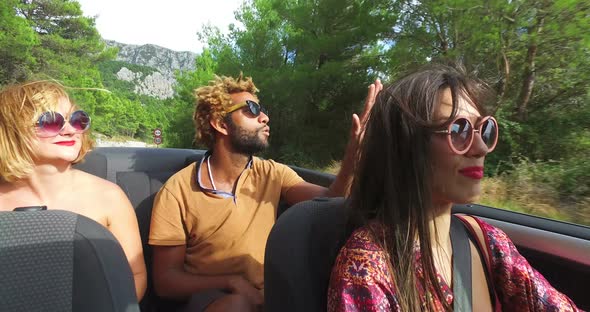 Beautiful young woman smiling and enjoying driving her friends in convertible