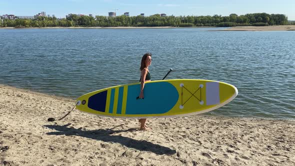 Caucasian Woman Walks Along the Beach and Carries a Sup Board on the River in the City