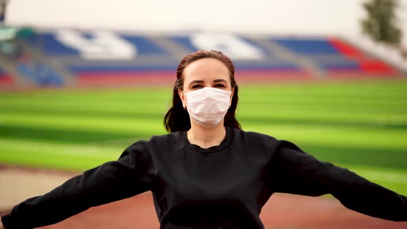 Young Woman in Medical Mask Doing Warm-up at Stadium, Adult Female in Black Casual Clothes Doing