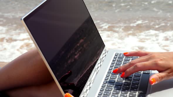 Close-up, Female Hands with Bright Orange Nails Typing on Laptop, on Beach By the Sea. Sea Is