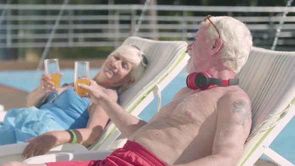 Mature Couple Lying on Sunbeds Near the Pool Drinking Juice, Talking and Smiling