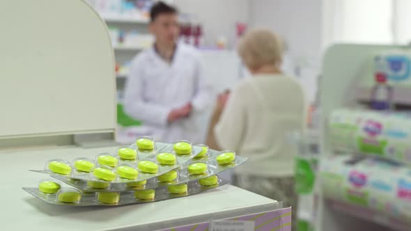 Pharmacist Talking To Senior Client, Pills Blisters on Foreground